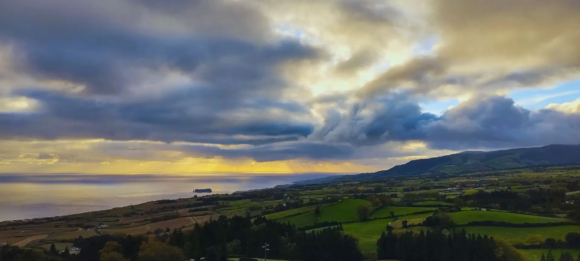 View of the coast of an island with an islet nearby and cloudy skies.