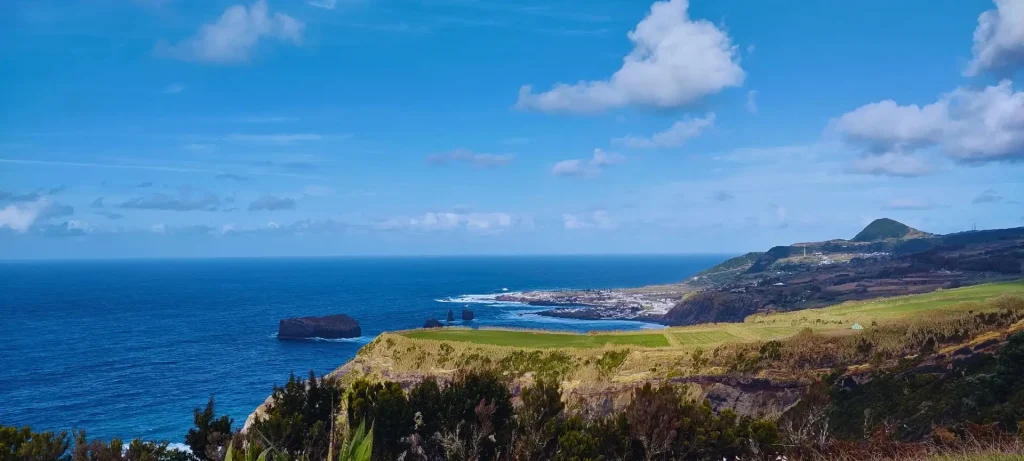 View of the coast of an island with a town and a few islets a little off the coast.