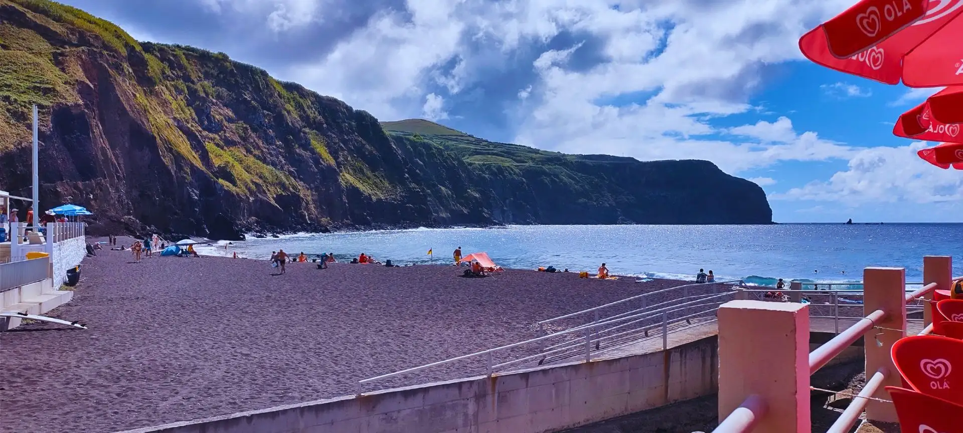 A dark sand beach with a long cliff meeting the sea to its left.