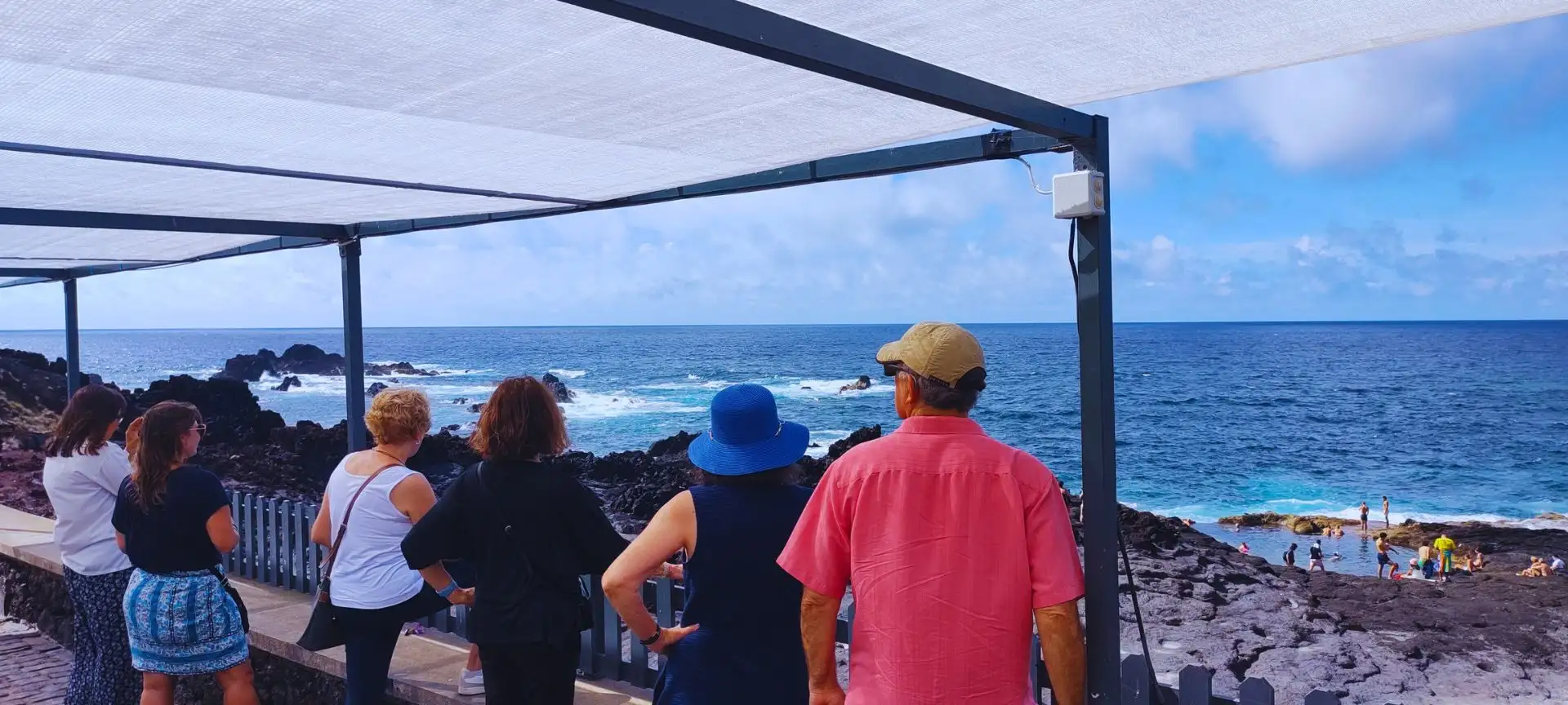 A group of visitors contemplating the view of the sea and natural pools, where people are bathing.