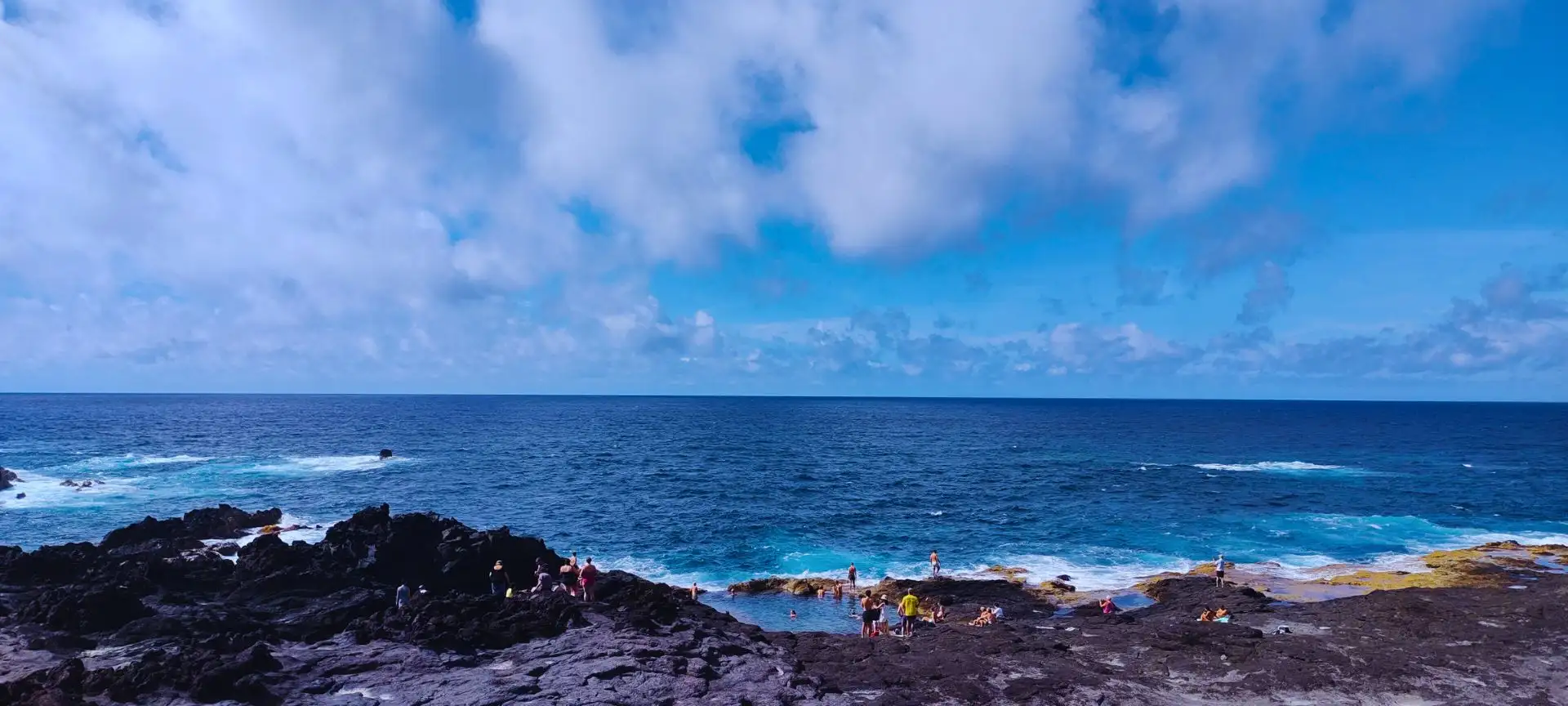 Natural pools with people bathing in them and the sea right next to the rocky coast.