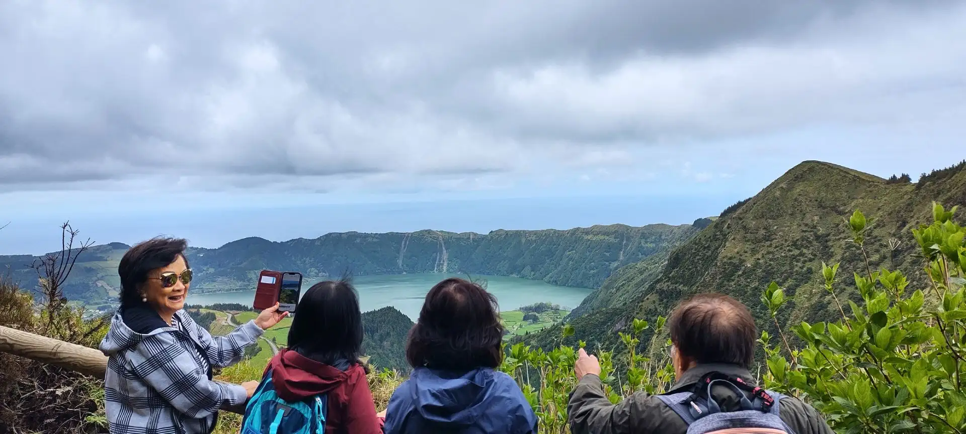 A group of tourists taking and sharing photos of the landscape seen from a viewpoint.