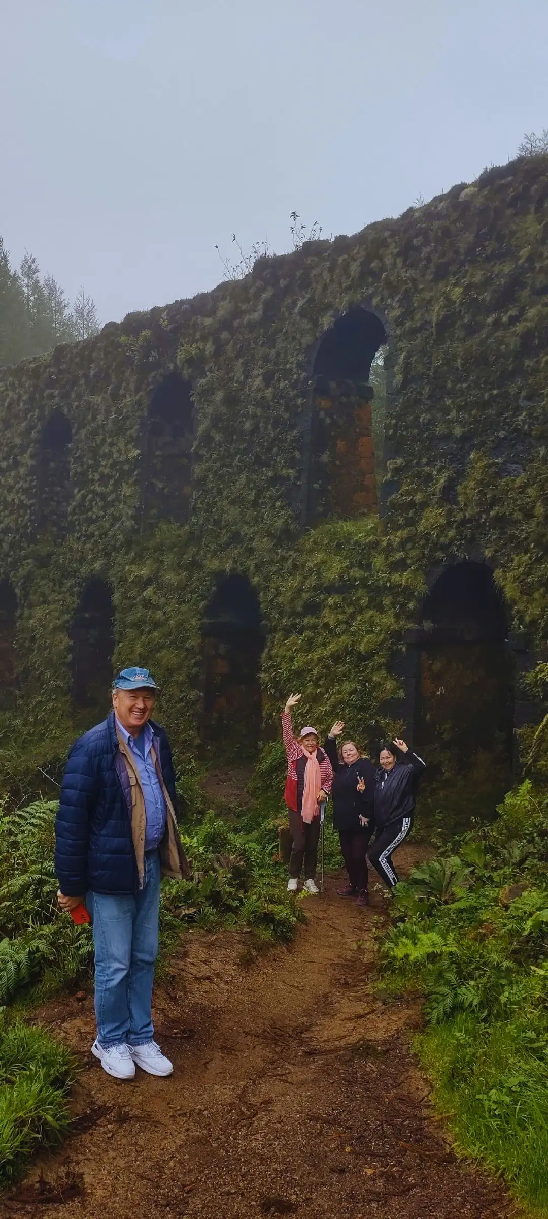 A group of tourists take a photo in front of a old aqueduct.